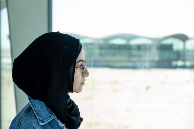 Foto jonge arabische vrouw met haar paspoort op de luchthaven klaar voor een nieuw avontuur met vliegtuig op de achtergrond