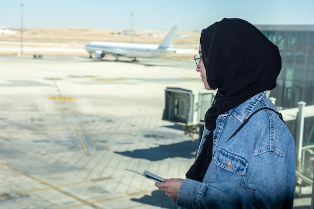 Jonge Arabische vrouw met haar paspoort op de luchthaven klaar voor een nieuw avontuur met vliegtuig op de achtergrond