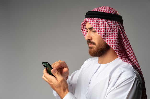 Jonge Arabische zakenman die smartphone op grijze achtergrond gebruikt