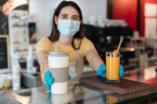 Jonge arbeidersvrouw die afhaalbestelling levert aan klant in coffeeshop tijdens uitbraak van coronavirus