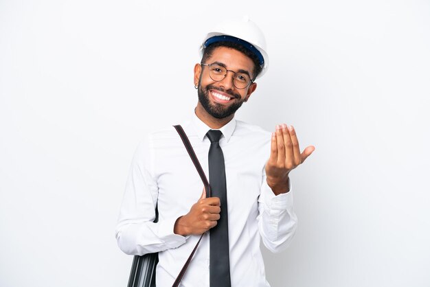 Jonge architect Braziliaanse man met helm en met blauwdrukken geïsoleerd op een witte achtergrond, uitnodigend om met de hand te komen Blij dat je bent gekomen