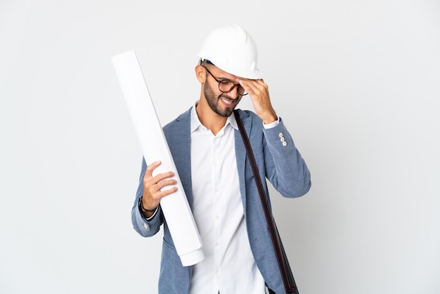 Jonge architect man met helm en blauwdrukken geïsoleerd op een witte muur met hoofdpijn te houden