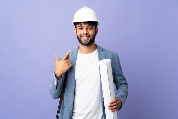 Jonge architect marokkaanse man met helm en blauwdrukken houden over geïsoleerd met een duim omhoog gebaar