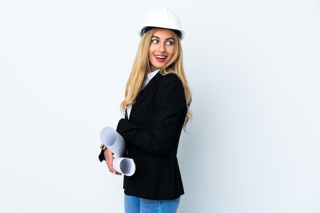 Jonge architect vrouw met helm en blauwdrukken houden geïsoleerd lachen