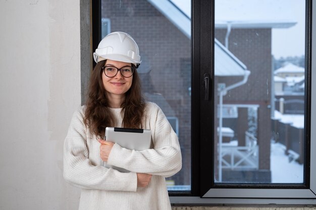 Foto jonge architectenvrouw met tablet die tijdens renovatie tegen de muur staat in een nieuw gebouw