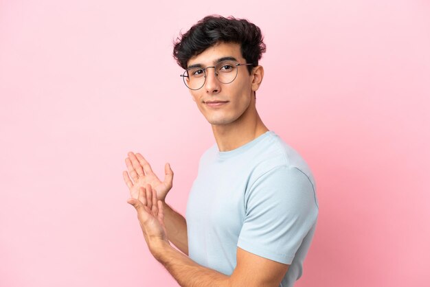 Jonge Argentijnse man geïsoleerd op roze achtergrond met een bril en iets presenteren