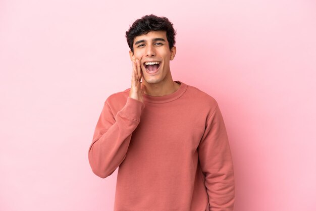 Jonge Argentijnse man geïsoleerd op roze achtergrond schreeuwen met wijd open mond