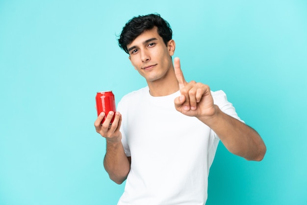 Jonge Argentijnse man met een verfrissing geïsoleerd op een blauwe achtergrond die een vinger laat zien en optilt