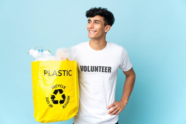 Jonge Argentijnse man met een zak vol plastic poseren met armen op heup en glimlachend