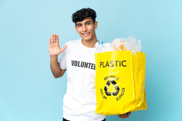 Jonge Argentijnse man met een zak vol plastic saluerend met de hand met een gelukkige uitdrukking