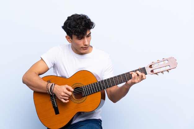 Jonge Argentijnse man met gitaar over geïsoleerde blauwe muur