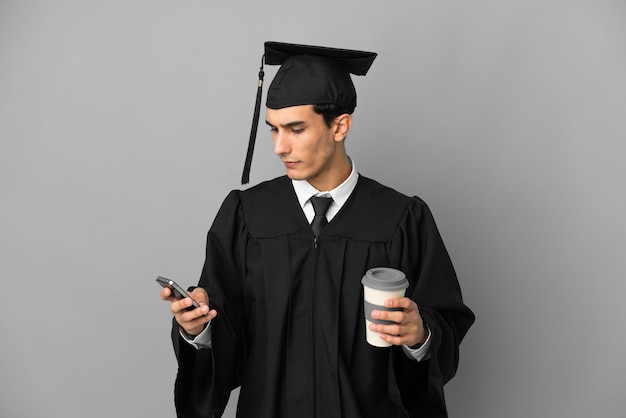 Jonge Argentijnse universitair afgestudeerde geïsoleerd op een grijze achtergrond met koffie om mee te nemen en een mobiel