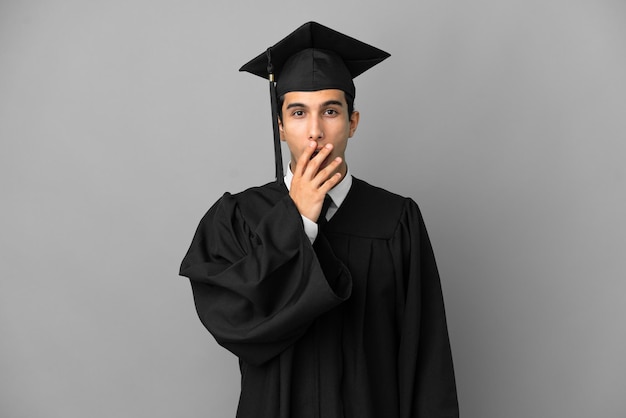 Jonge argentijnse universitair afgestudeerde geïsoleerd op een grijze achtergrond verrast en geschokt terwijl hij naar rechts kijkt