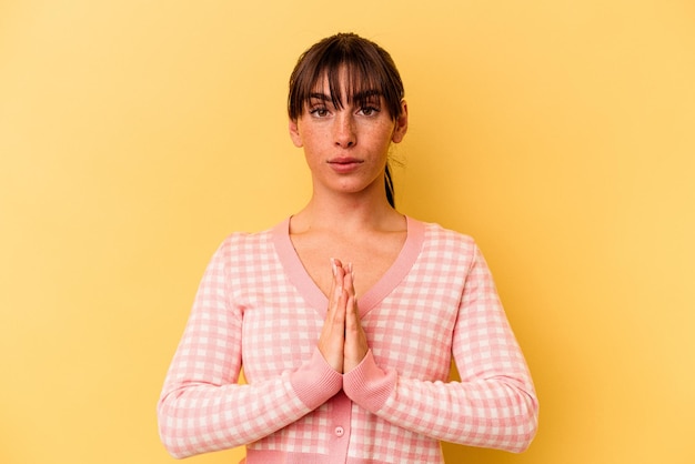 Jonge Argentijnse vrouw geïsoleerd op gele achtergrond bidden, met toewijding, religieuze persoon op zoek naar goddelijke inspiratie.