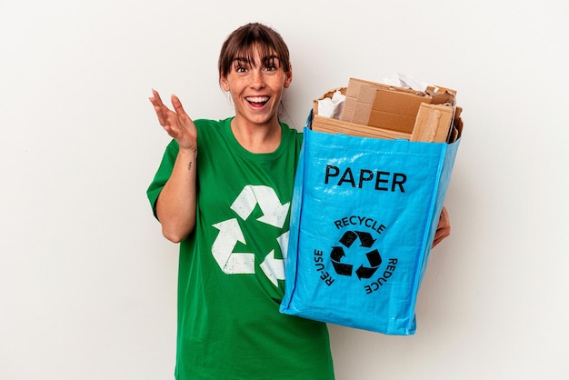 Jonge Argentijnse vrouw gerecycled papier geïsoleerd op gele achtergrond ontvangt een aangename verrassing, opgewonden en steekt handen op.