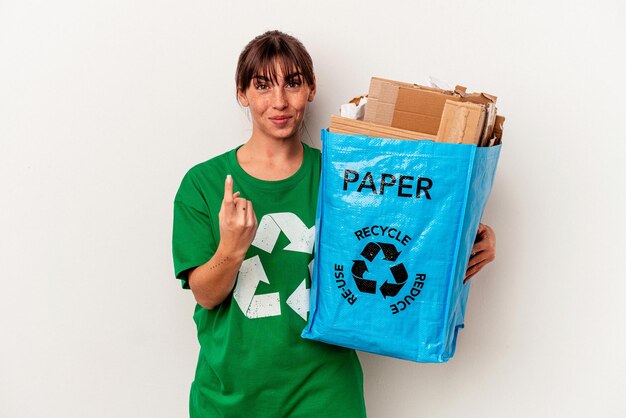 Jonge Argentijnse vrouw gerecycled papier geïsoleerd op gele achtergrond wijzend met de vinger naar je alsof uitnodigend dichterbij komt.