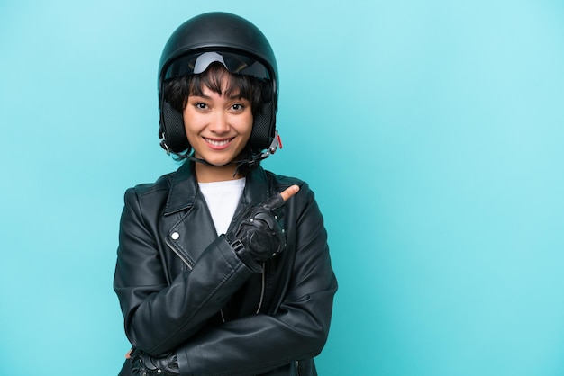 Jonge Argentijnse vrouw met een motorhelm geïsoleerd op een blauwe achtergrond die naar de zijkant wijst om een product te presenteren