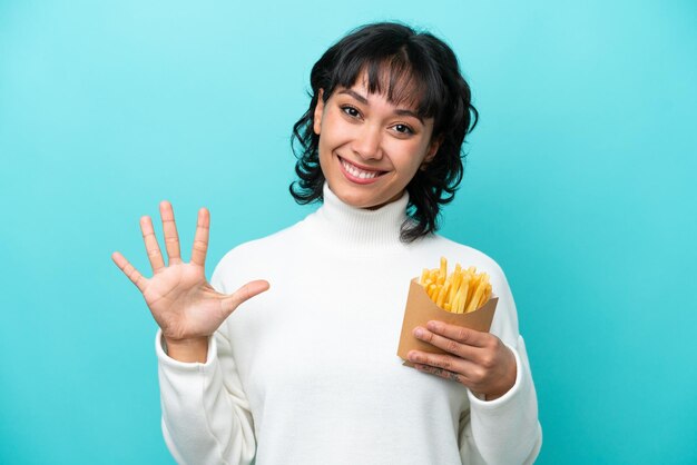 Jonge Argentijnse vrouw met gefrituurde chips geïsoleerd op blauwe achtergrond die vijf met vingers telt