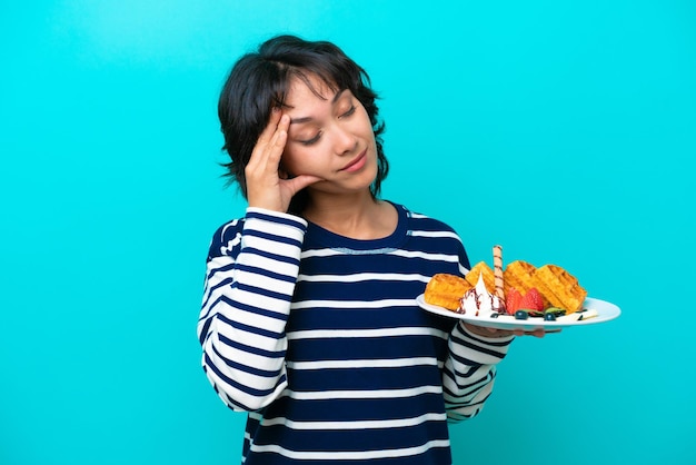 Jonge argentijnse vrouw met wafels geïsoleerd op blauwe achtergrond met hoofdpijn