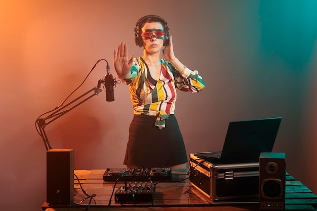 Jonge artiest doet stopbord met palm en luistert naar geluiden in koptelefoons, mixt muziek op draaitafels. Coole vrouwelijke DJ die afwijzing en ontkenningsgebaar toont, verboden of weigering.