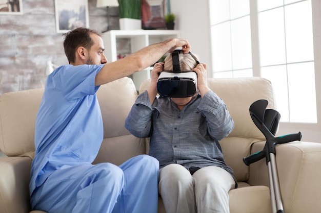 Jonge arts die een virtual reality-bril op een oudere vrouw in een verpleeghuis zet.