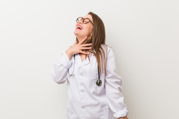 Jonge arts vrouw tegen een witte muur lacht hardop hand op de borst te houden.