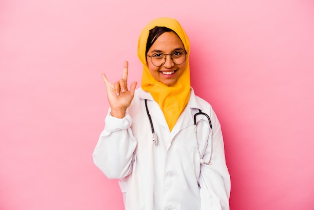 Jonge artsen moslimvrouw die op roze muur wordt geïsoleerd die een hoornsgebaar toont als revolutieconcept.
