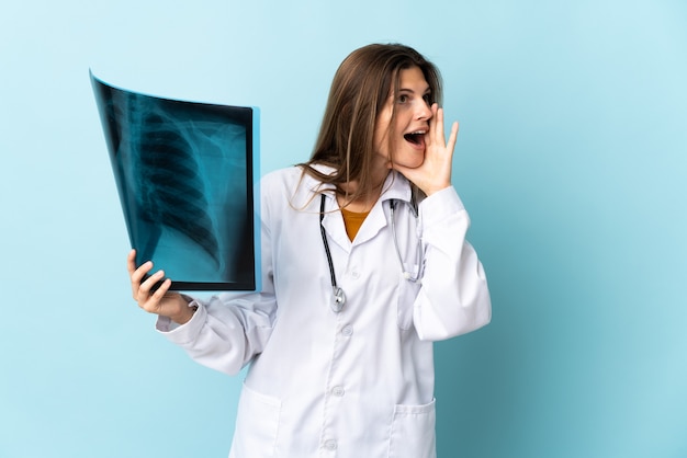 Jonge artsenvrouw die radiografie over geïsoleerde muur houdt die met wijd open mond aan de zijkant schreeuwt