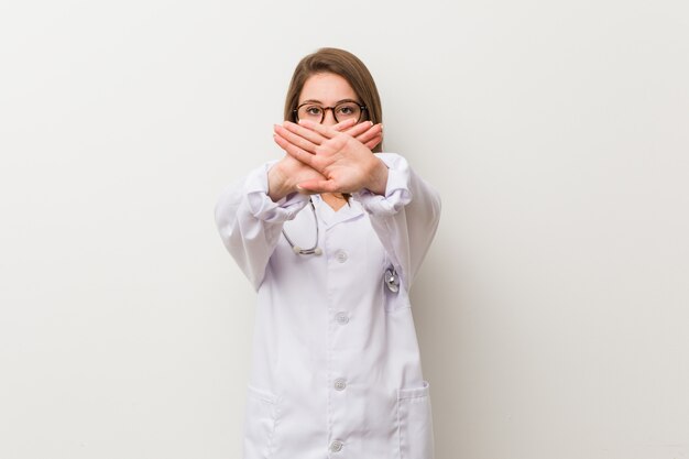 Jonge artsenvrouw tegen een witte muur die een ontkenningsgebaar doet