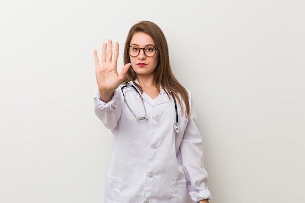 Jonge artsenvrouw tegen een witte muur die zich met uitgestrekte hand bevinden die eindeteken tonen