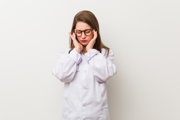 Jonge artsenvrouw tegen een witte muur wat betreft tempels en het hebben van hoofdpijn.