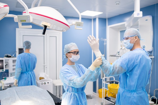 Jonge assistent rubberen handschoenen zetten handen van chirurg tijdens de voorbereiding voor operatie in het ziekenhuis