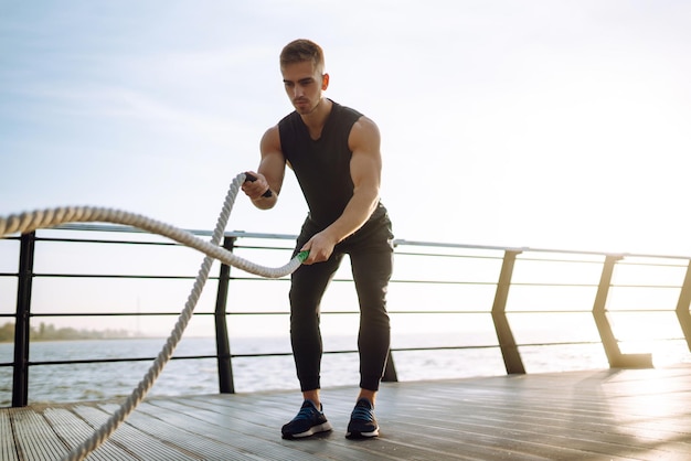 Jonge atleet die sportkleding draagt, doet training op de strandpier Man doet oefeningen buitenshuis