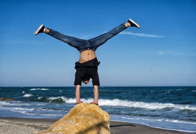 Jonge atleet doet handstand op de steen van het strand. Straat training. Evenwichtsconcept.