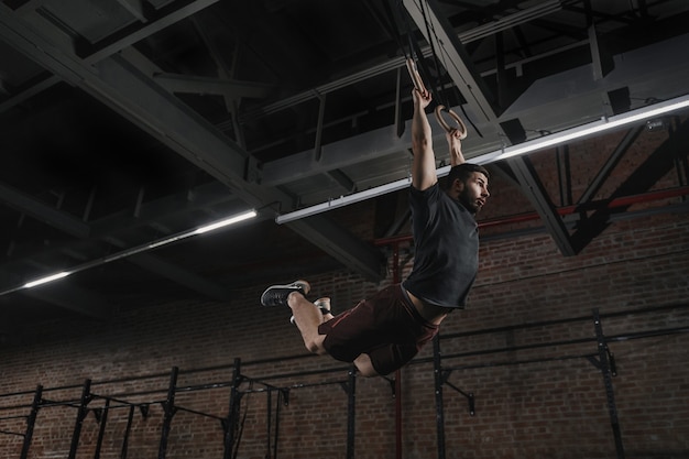 Jonge atleet doet pull-ups op gymnastische ringen bij cross fit gym. knappe man beoefenen van spier-ups swingende training oefening.