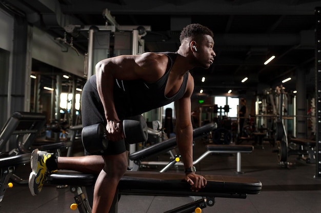 Jonge atletische Afro-Amerikaanse man traint in een donkere sportschool. Atletische man tillen zware halters.