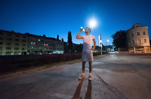 jonge atletische man die water drinkt na een nachtelijke hardloopsessie in de stad