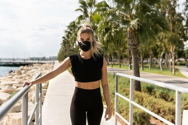 Jonge atletische vrouw die een gezichtsmasker draagt tijdens haar straattraining in de zomer