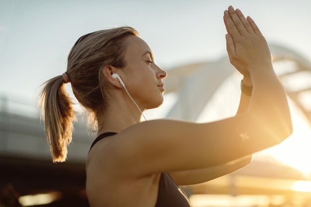 Jonge atletische vrouw die mediteert met gesloten ogen bij zonsondergang