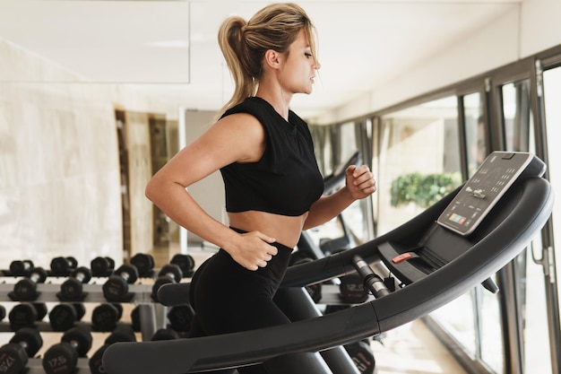 Jonge atletische vrouw die op de loopband loopt tijdens fitnesstraining