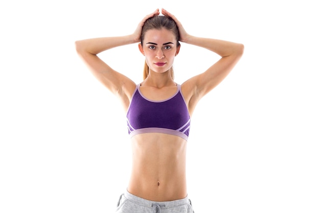 Jonge atletische vrouw, gekleed in een paarse sporttop en grijze korte broek met een paardenstaart die haar hoofd vasthoudt