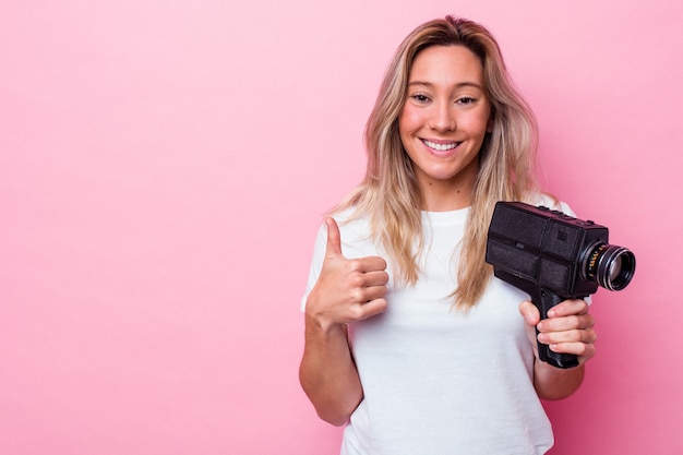 Jonge australische vrouw filmen met een vintage videocamera geïsoleerd glimlachend en duim omhoog