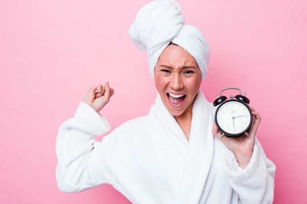 Jonge australische vrouw verlaat de douche laat geïsoleerd op roze achtergrond die vuist opheft na een overwinning, winnaarconcept.