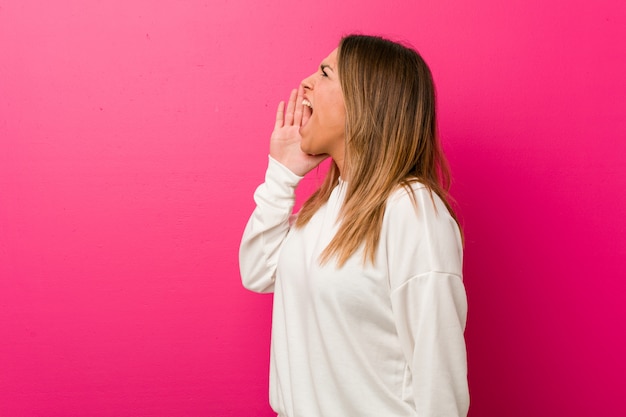 Jonge authentieke charismatische echte mensenvrouw tegen een muur die en palm dichtbij geopende mond schreeuwen houden.