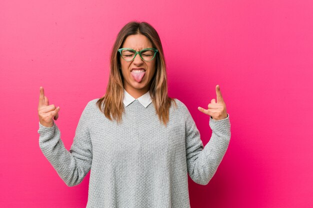 Jonge authentieke charismatische echte mensenvrouw tegen een muur die rotsgebaar met vingers tonen