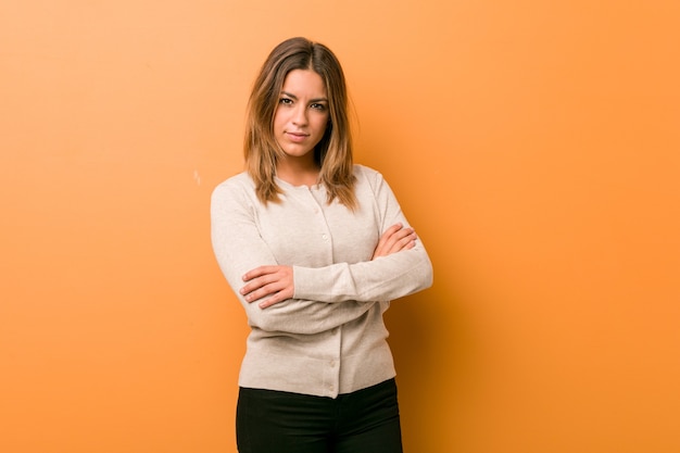 Jonge authentieke charismatische echte mensenvrouw tegen een muur die zich zelfverzekerd voelt en vastberaden de armen over elkaar slaat.