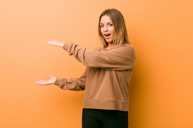 Jonge authentieke charismatische echte mensenvrouw tegen een muur geschokt en verbaasd met een kopie ruimte tussen handen.