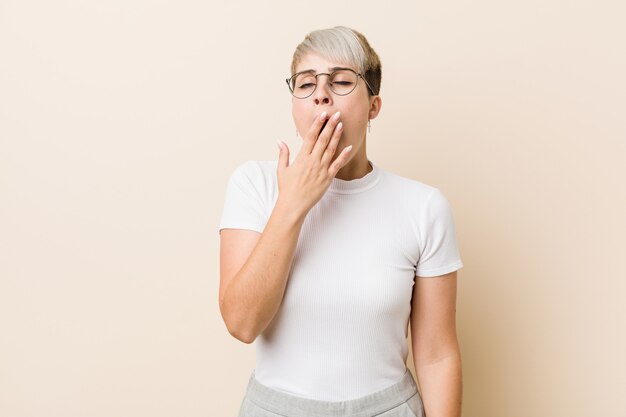 Jonge authentieke natuurlijke vrouw die een witte overhemd geeuw draagt die een vermoeid gebaar toont dat mond behandelt met hand.