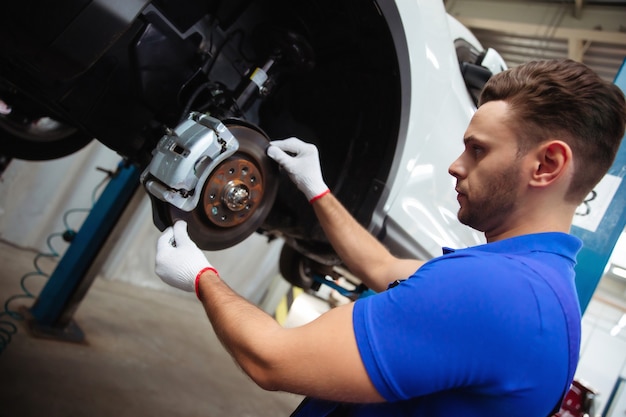 Jonge automonteur in een speciaal pak repareert het remsysteem van een auto of verandert de remblokken