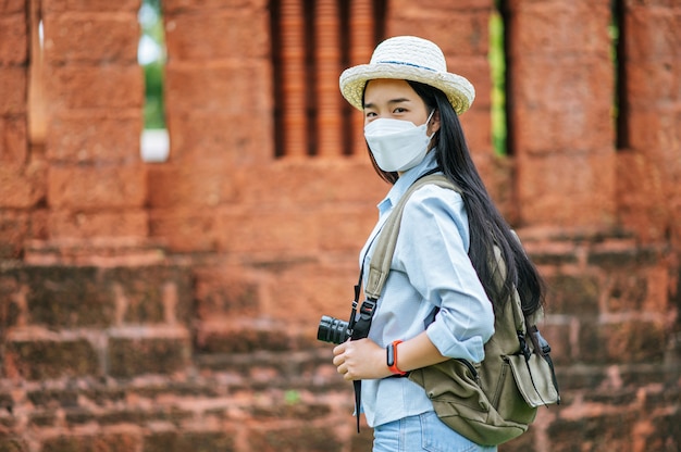 Jonge Aziatische backpacker-vrouw met hoed en beschermingsmasker tijdens het reizen op een historische plek